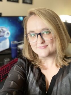 Amie Croteau poses in front of her desk, with her computer in the background.